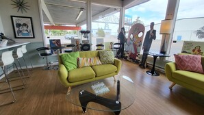 A modern living room with a green sofa, a glass coffee table, and a chess set. There are white bar stools and a bar area with a popcorn machine.