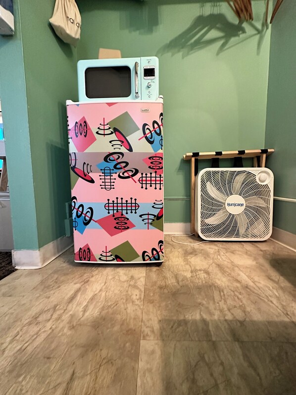 A refrigerator with a colorful geometric pattern, a microwave on top, and a small fan labeled "Hurricane" beside it. - Atomic Motel (Astoria)