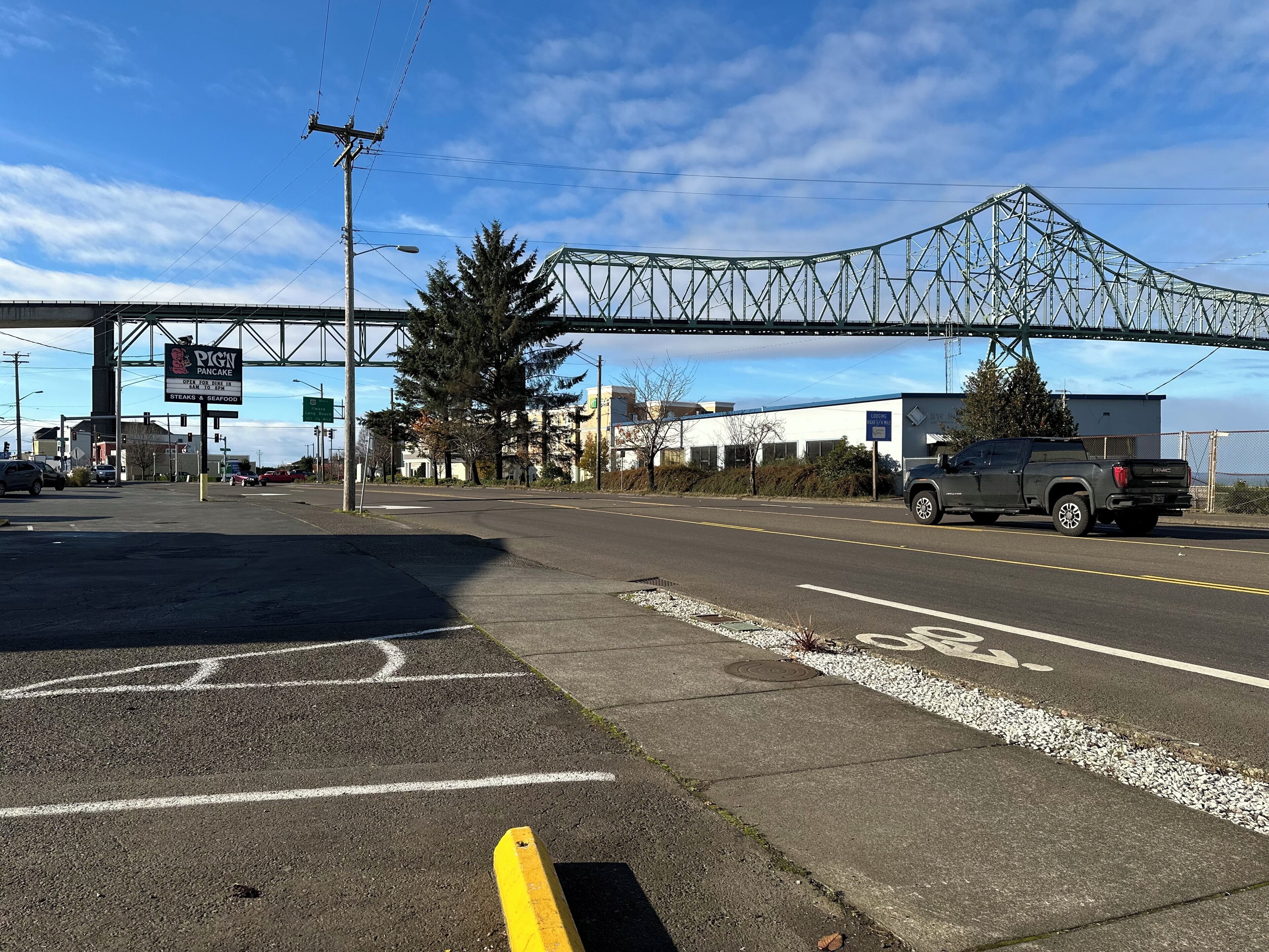 A parking lot with a yellow curb, a pedestrian crossing, and a bridge overhead.