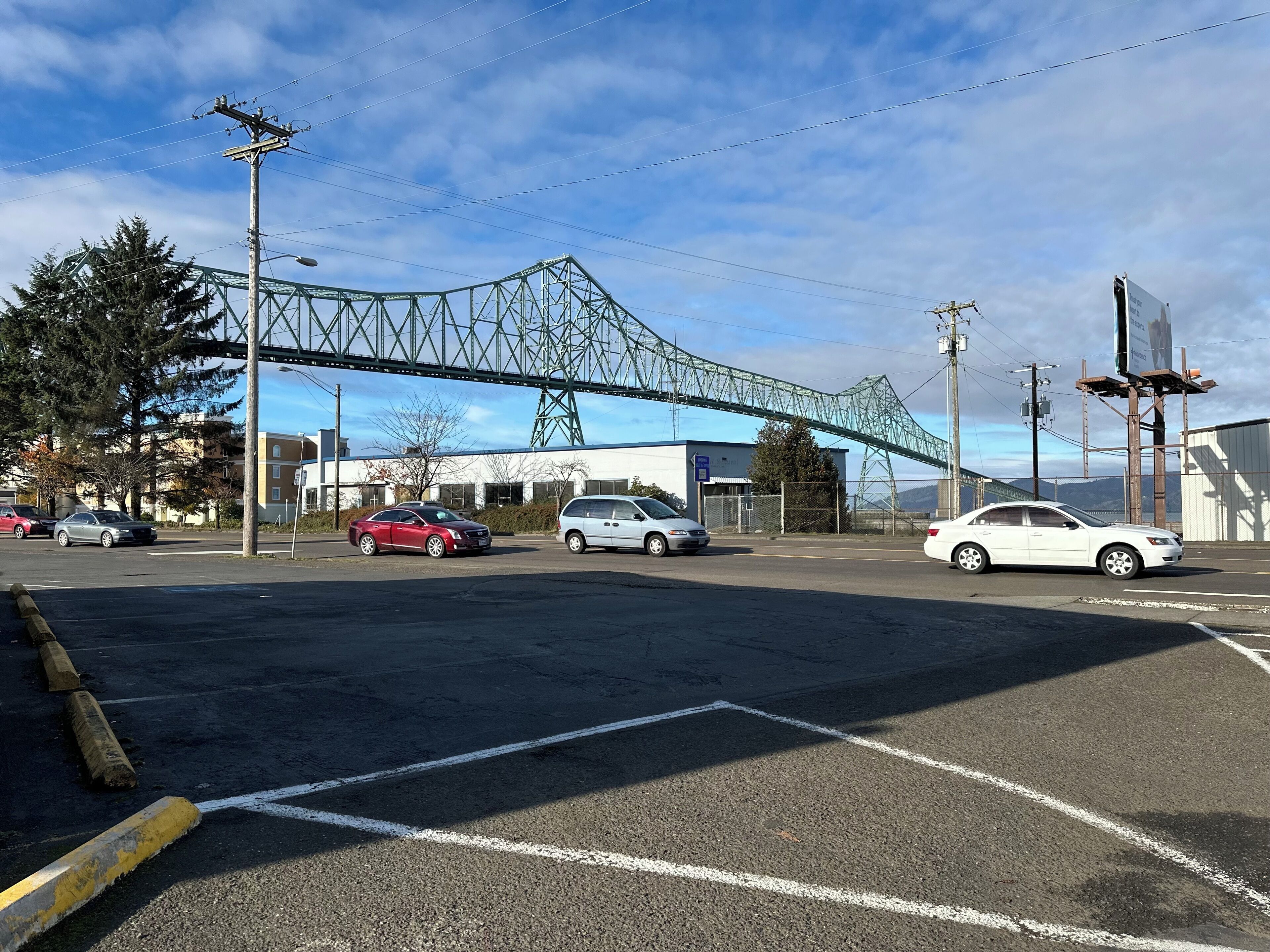 A parking lot with cars, a bridge, and buildings in the background.
