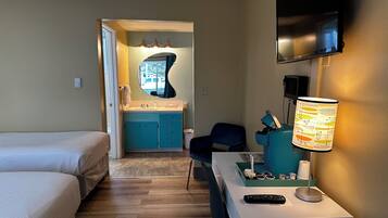Habitación de hotel con cama, escritorio con lámpara, televisión y baño visible a través de una puerta abierta.