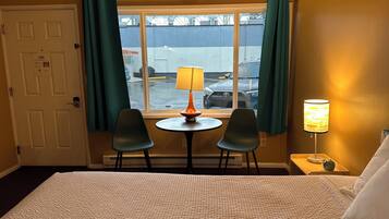Een hotelkamer met een bed, twee stoelen, een tafeltje met een lamp en een raam met gordijnen.