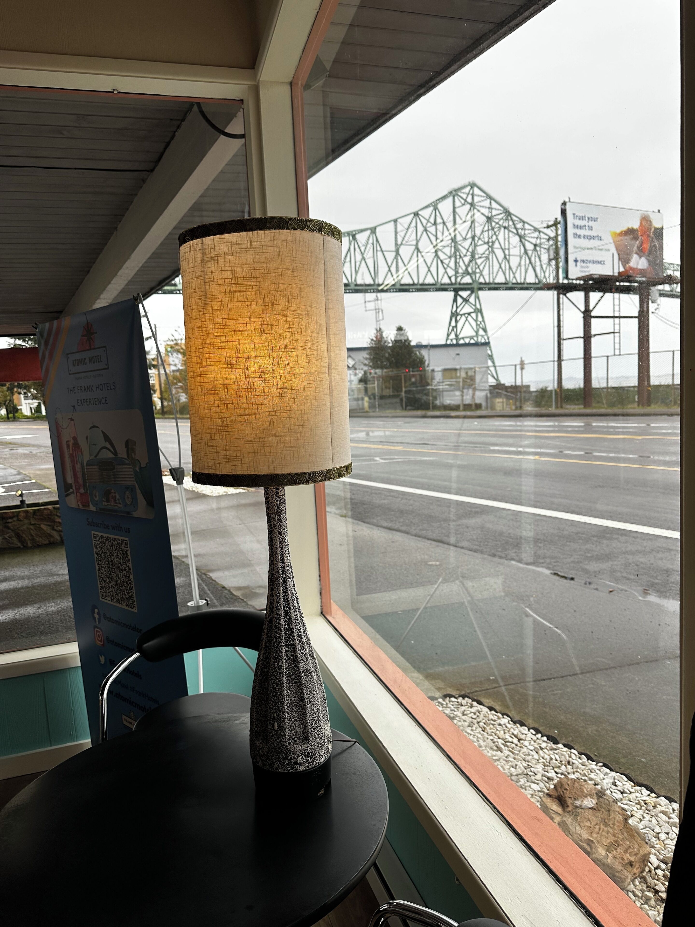 A table with a textured lamp, a QR code sign, and a view of a bridge and road outside.