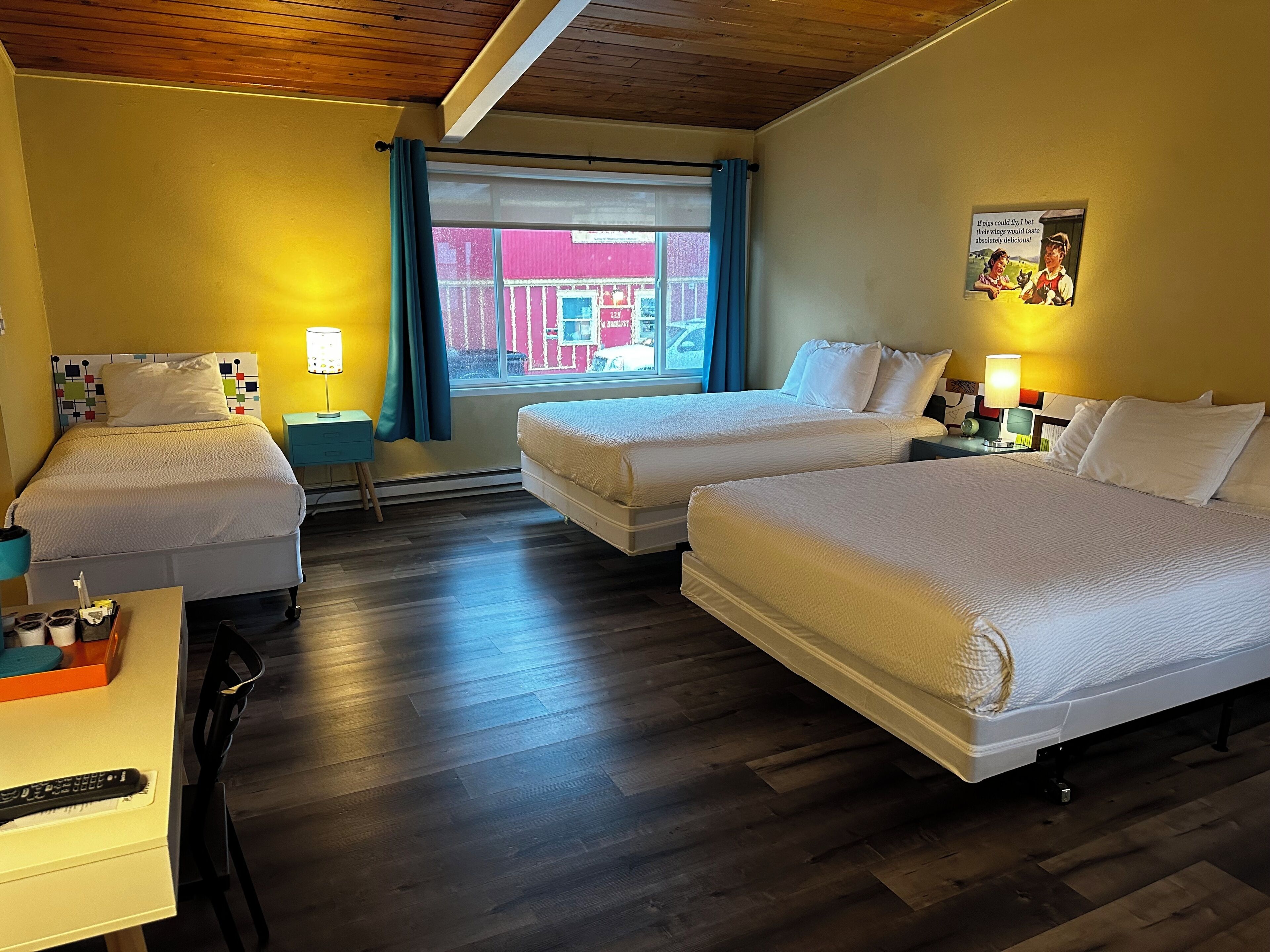 Habitación de hotel con dos camas, una ventana con cortinas azules, techo de madera y un cartel en la pared.
