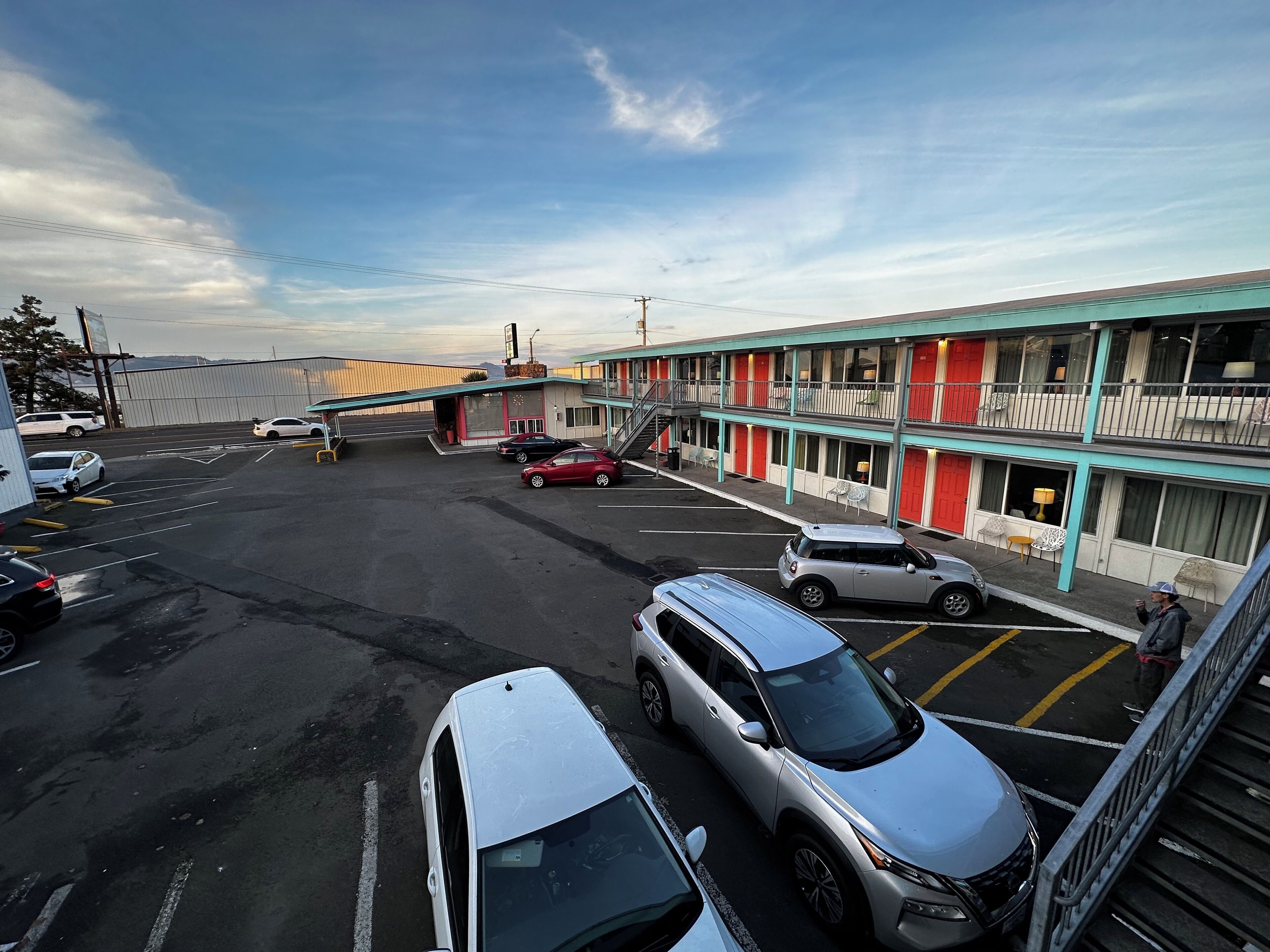 Een motel met een tweelaags gebouw, meerdere parkeerplaatsen en een heldere lucht.