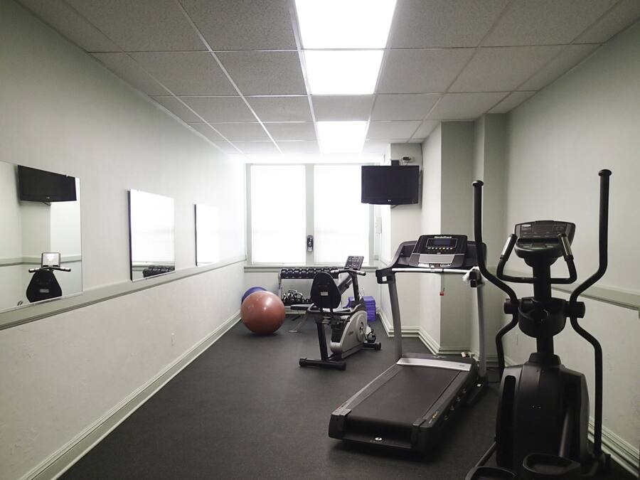A fitness room with exercise equipment, a large mirror, and a television on the wall.