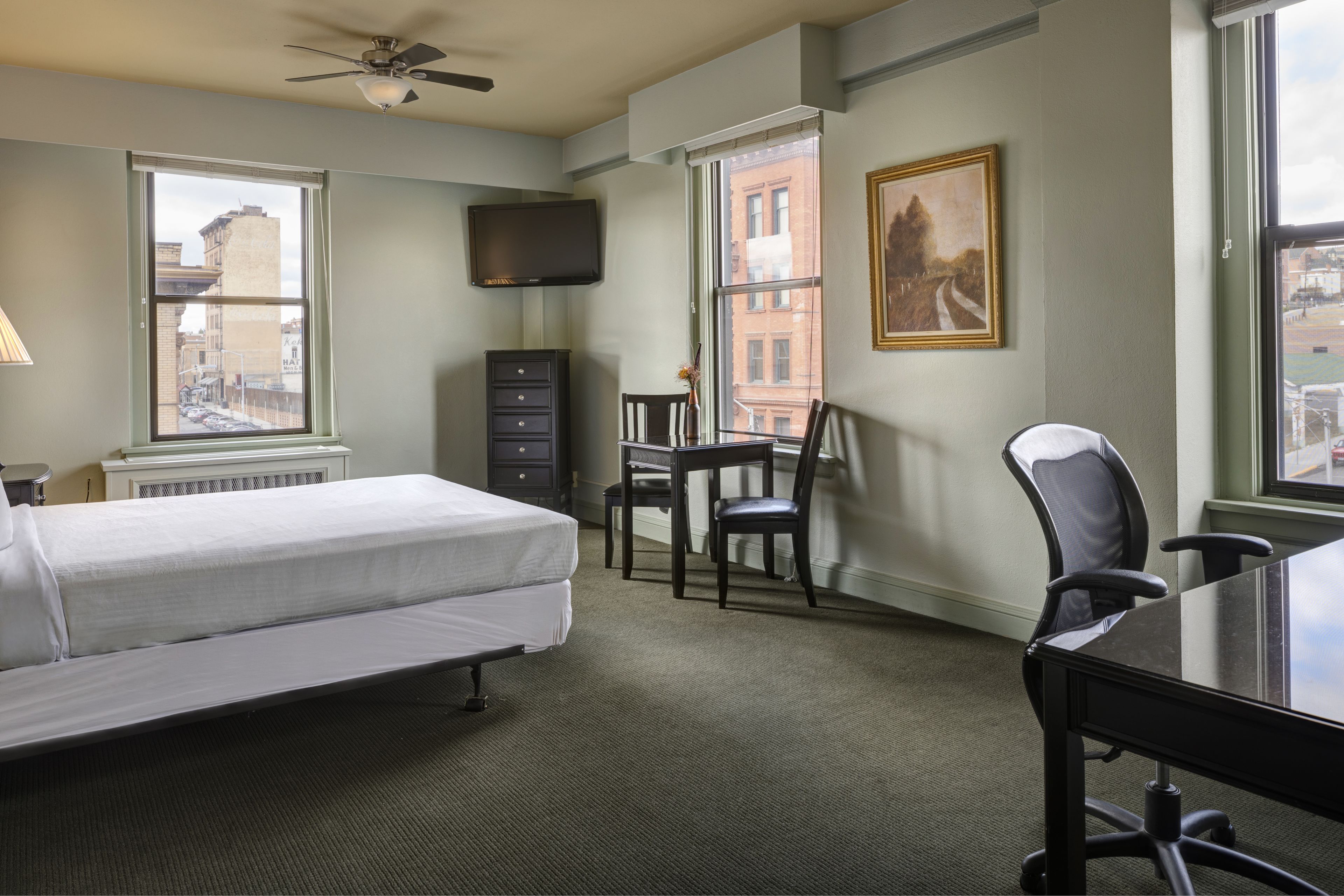 Ein Hotelzimmer mit Bett, Schreibtisch, Sessel, Fernseher und Fenster mit Blick auf die Stadt.