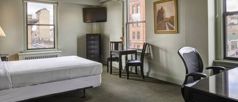 Ein Hotelzimmer mit Bett, Schreibtisch, Sessel, Fernseher und Fenster mit Blick auf die Stadt.