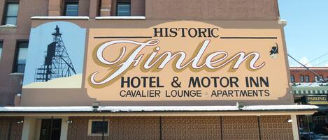 Un bâtiment sur lequel est apposée une grande enseigne indiquant le « Historic Finlen Hotel & Motor Inn », avec un design classique et une illustration mettant en valeur une tour imposante.