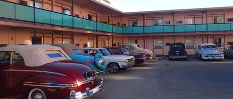 A parking lot with several vintage cars parked in front of a motel with a two-story structure and a flat roof.