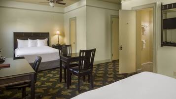 A hotel room with a bed, a desk, a chair, a ceiling fan, and a bathroom door.