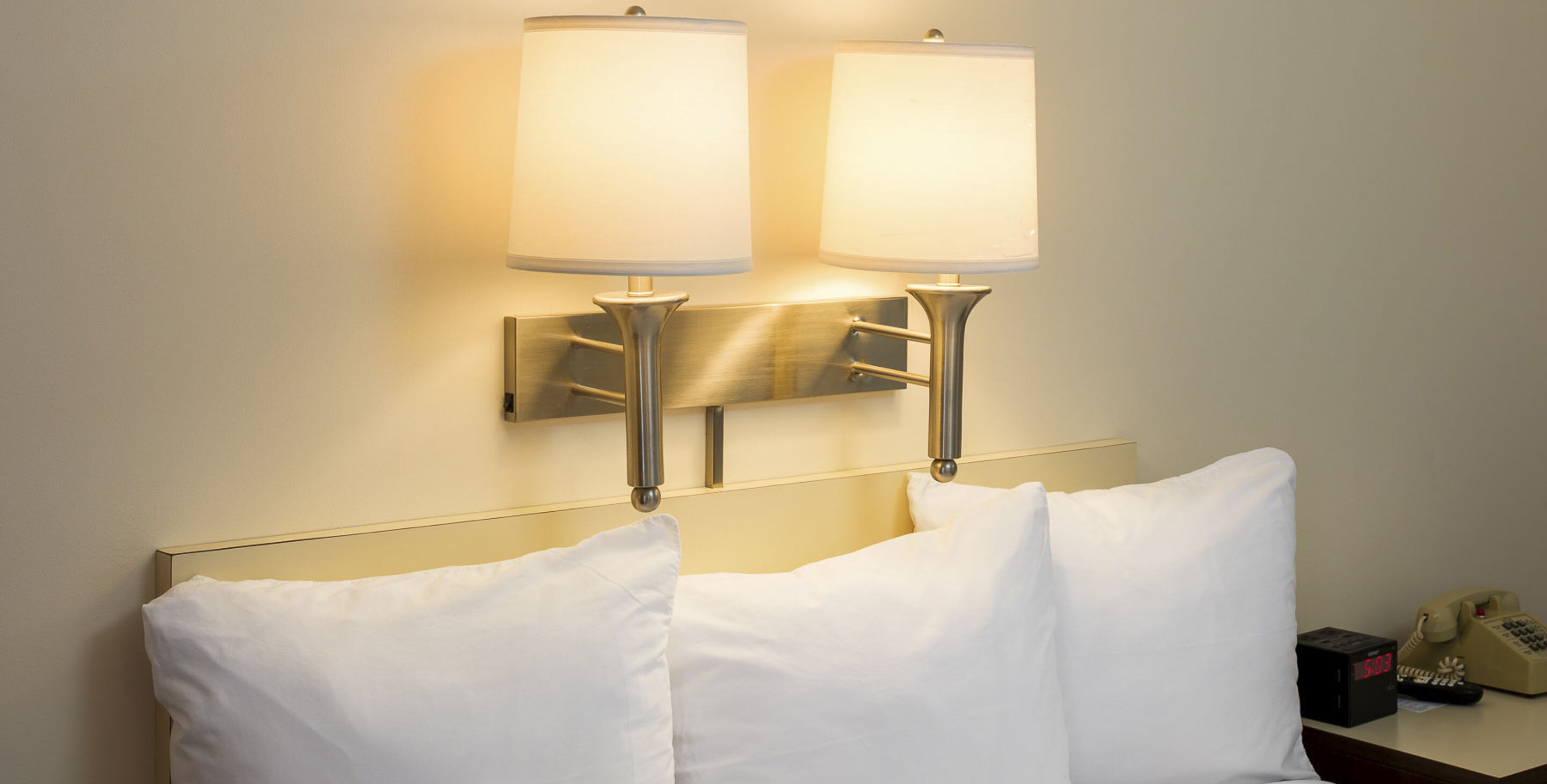 Ein Hotelzimmer mit zwei Nachttischlampen, einem Bett mit weißen Bettwäsche und einem Nachttisch mit Telefon und Wecker.