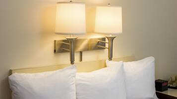 A hotel room with two bedside lamps, a bed with white linens, and a nightstand with a telephone and a clock.
