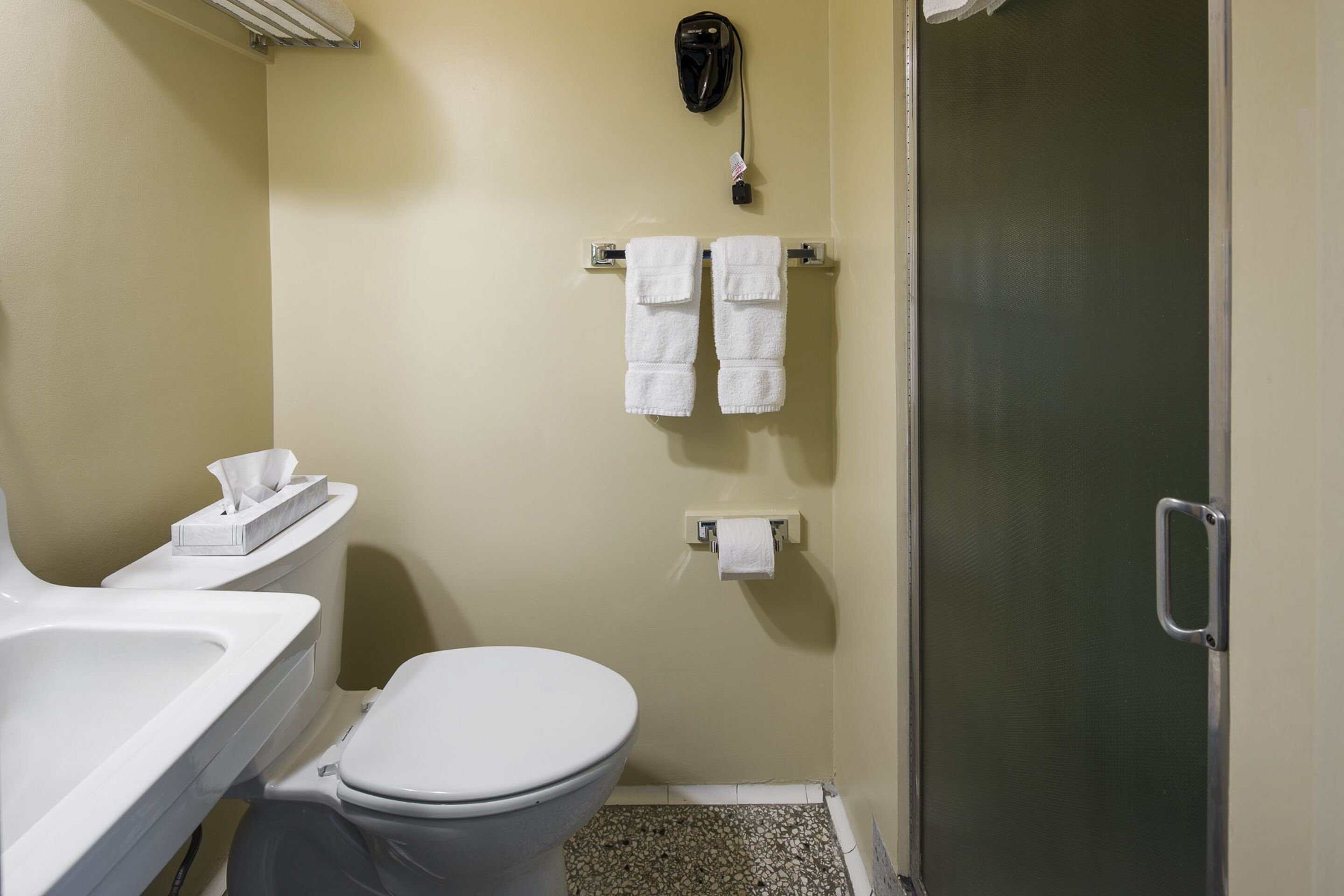 A bathroom with a toilet, sink, and shower. There are towels hanging on the wall.