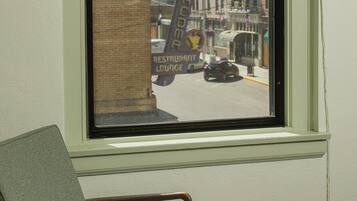 A room with a window overlooking a street, a chair, and a patterned carpet.