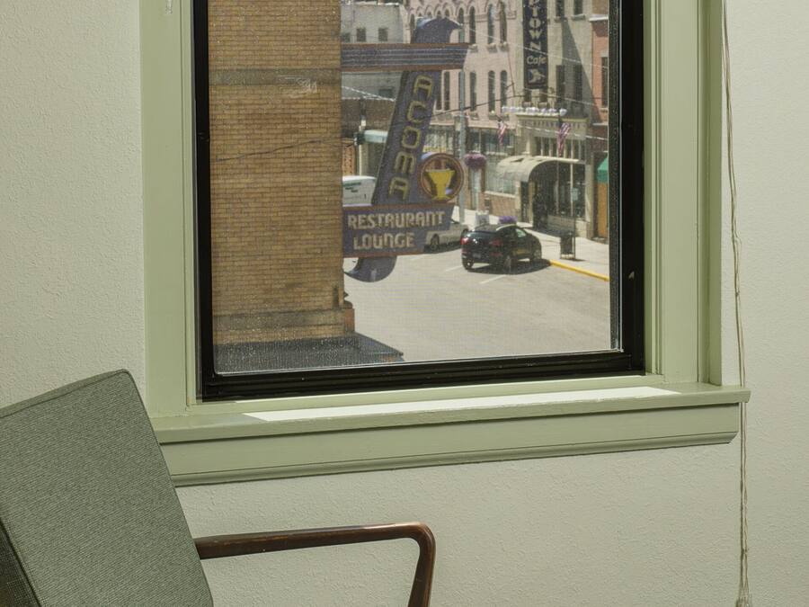 A room with a window overlooking a street, a chair, and a patterned carpet.