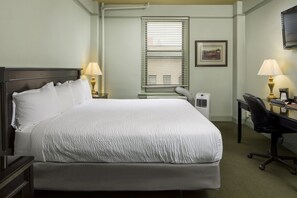 A hotel room with a large bed, two bedside lamps, a desk with a chair, a window with blinds, and a framed picture on the wall. - Finlen Hotel and Motor Inn (Butte)