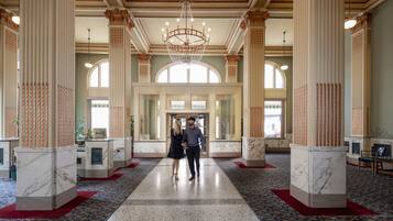 A grand lobby with marble columns, a chandelier, and a red carpeted floor.