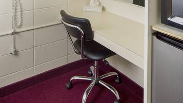 A room with a black office chair, a white desk, a telephone, and a television.
