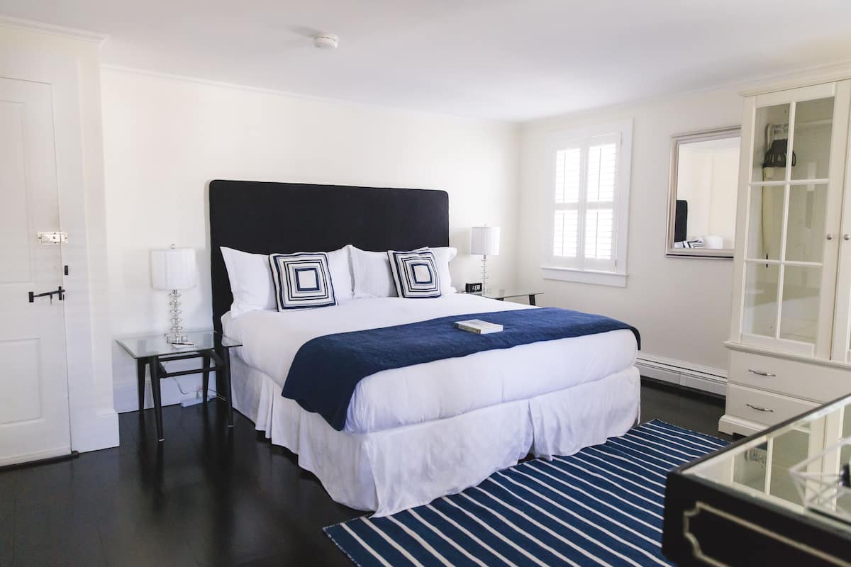 Habitación de hotel con una cama grande, dos mesitas de noche, un tocador, un aparador, un espejo y una ventana con persianas.