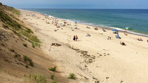 Ein weiter Sandstrand mit Menschen, die sonnenbaden und schwimmen, eine sanfte Böschung auf der einen Seite und ein ruhiges Meer.