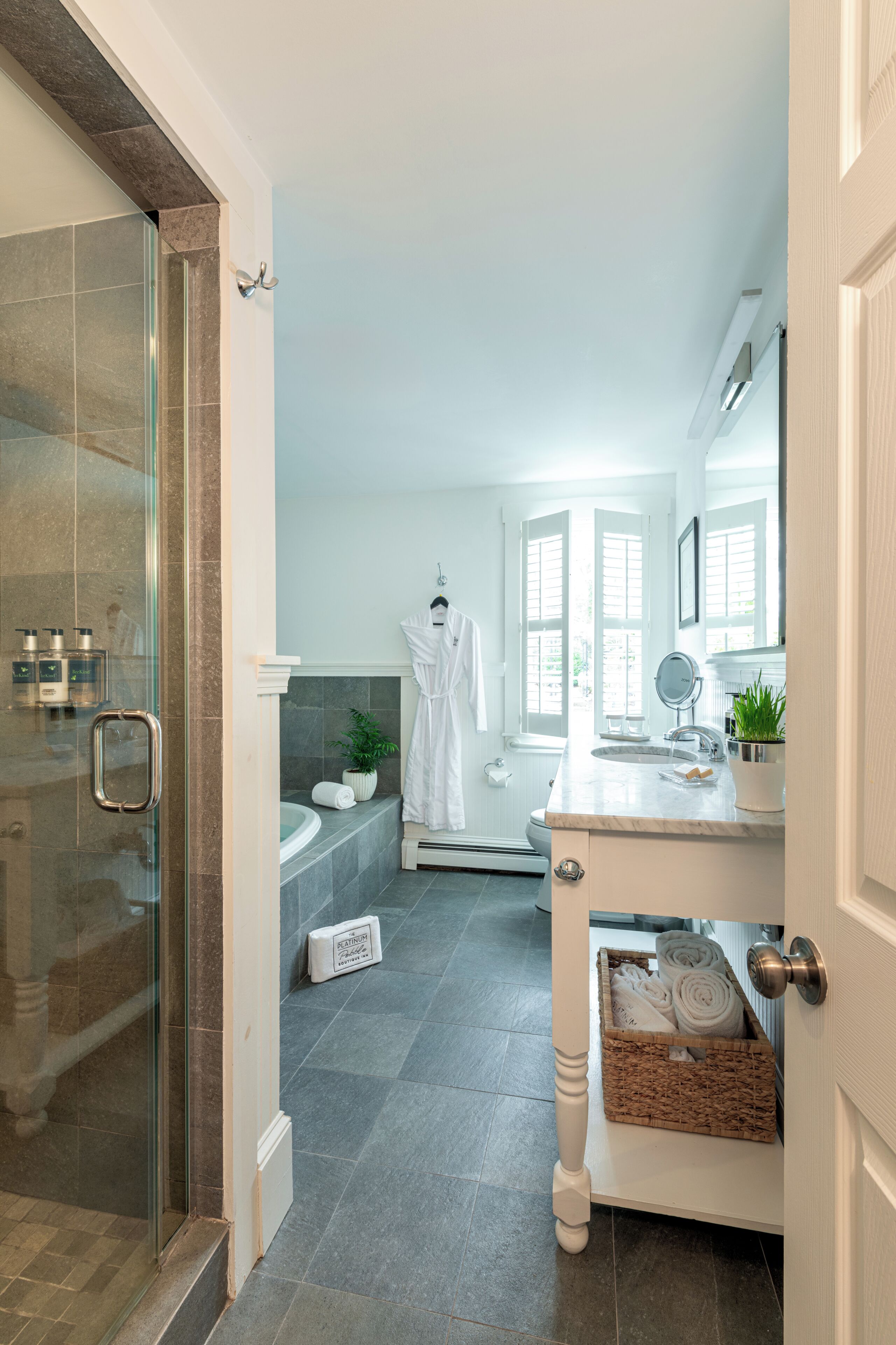 A modern bathroom with a glass shower enclosure, a bathtub, a sink with a marble countertop, and a potted plant.