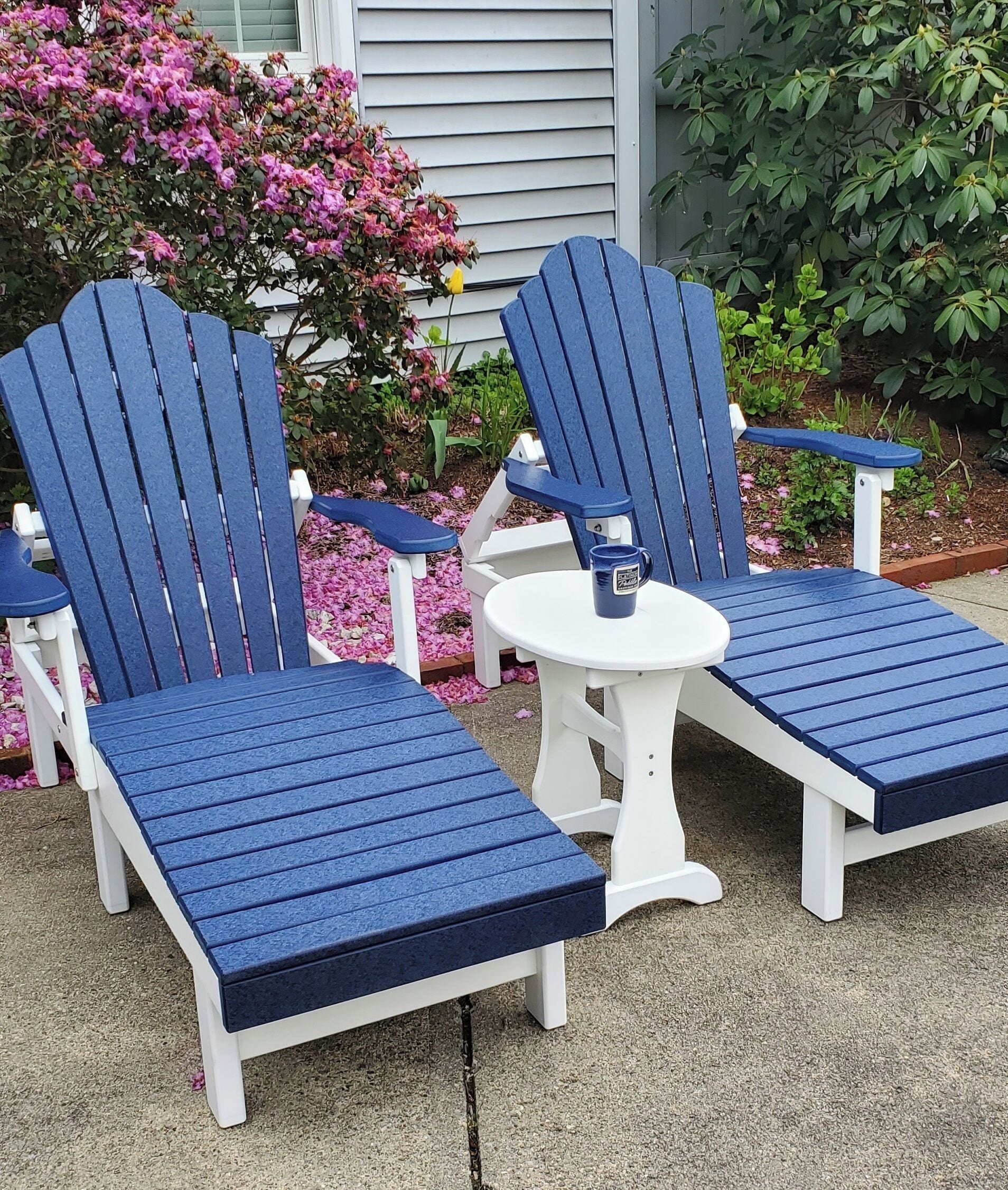 A set of Adirondack chairs with a small round table in a garden setting.