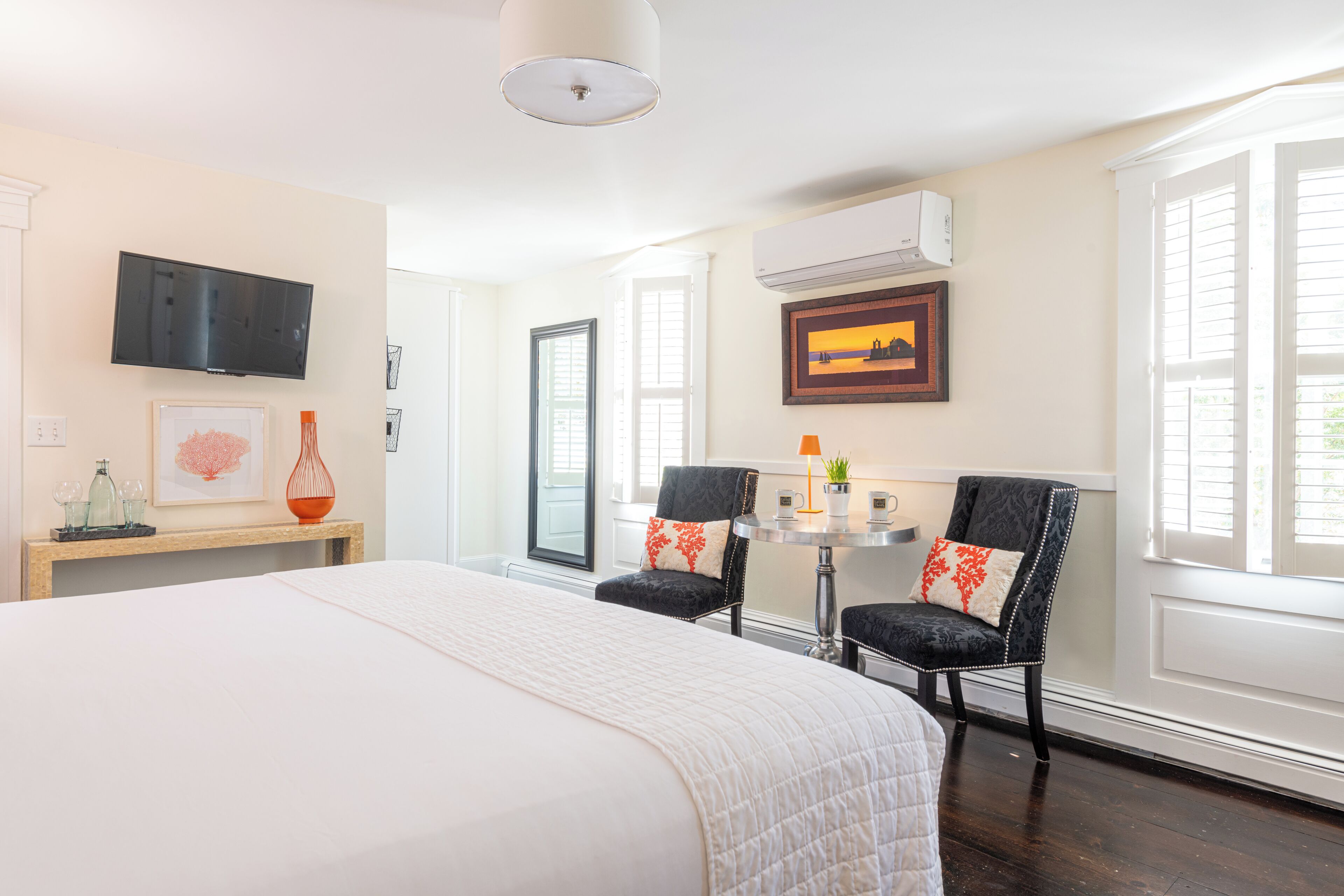 A hotel room with a bed, two chairs, a small table, a TV, and an air conditioning unit.