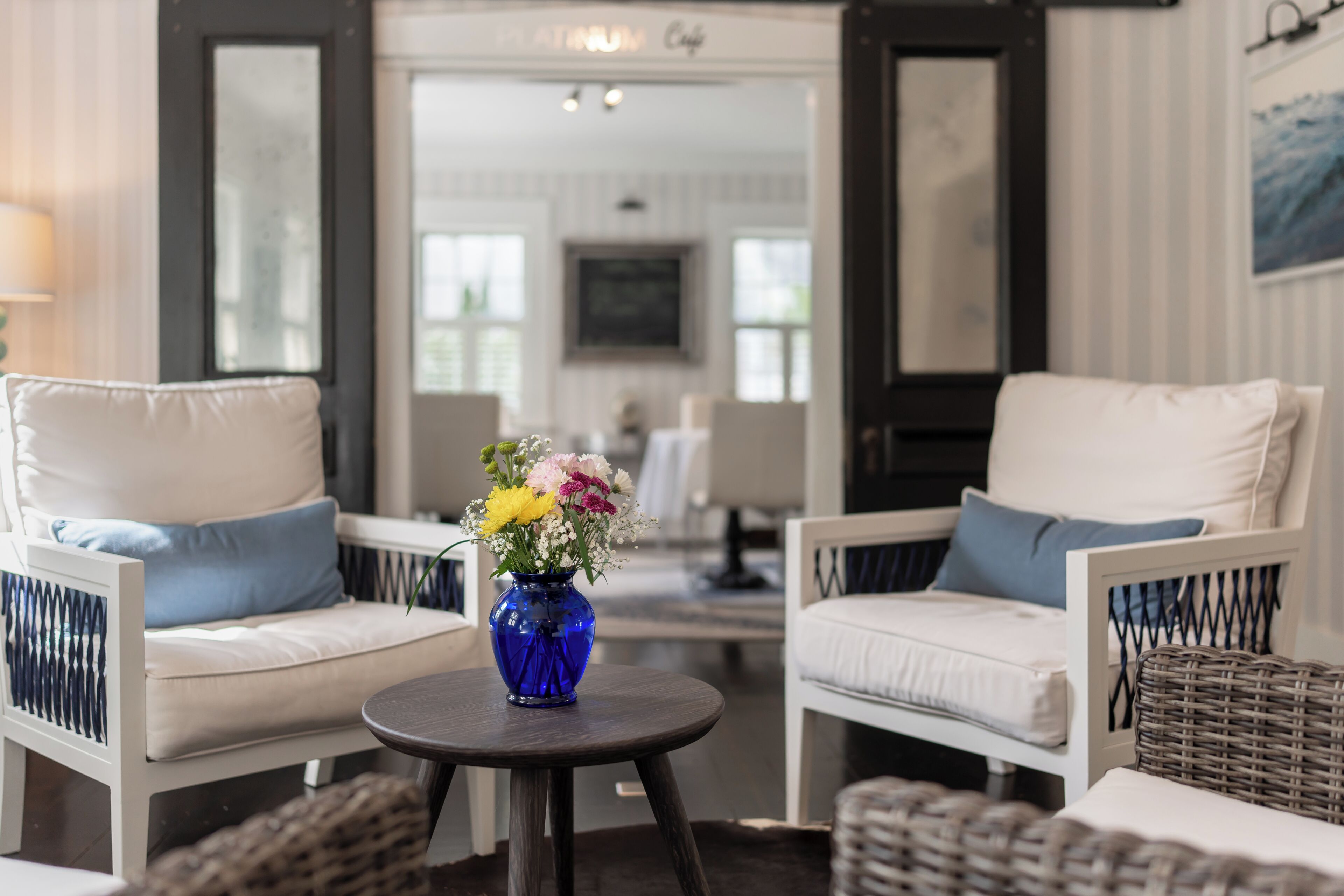 A room with two white sofas, a small round table with a blue vase of flowers, and wicker furniture.