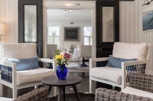 Una habitación con dos sofás blancos, una mesita redonda con un jarrón de flores azules y mobiliario de mimbre.