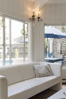 Un sofá blanco con un cojín estampado con un mapa, una ventana que da a una vista de un edificio y una lámpara colgante.