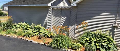A single-story house with a garage door, surrounded by a garden with various plants and flowers.