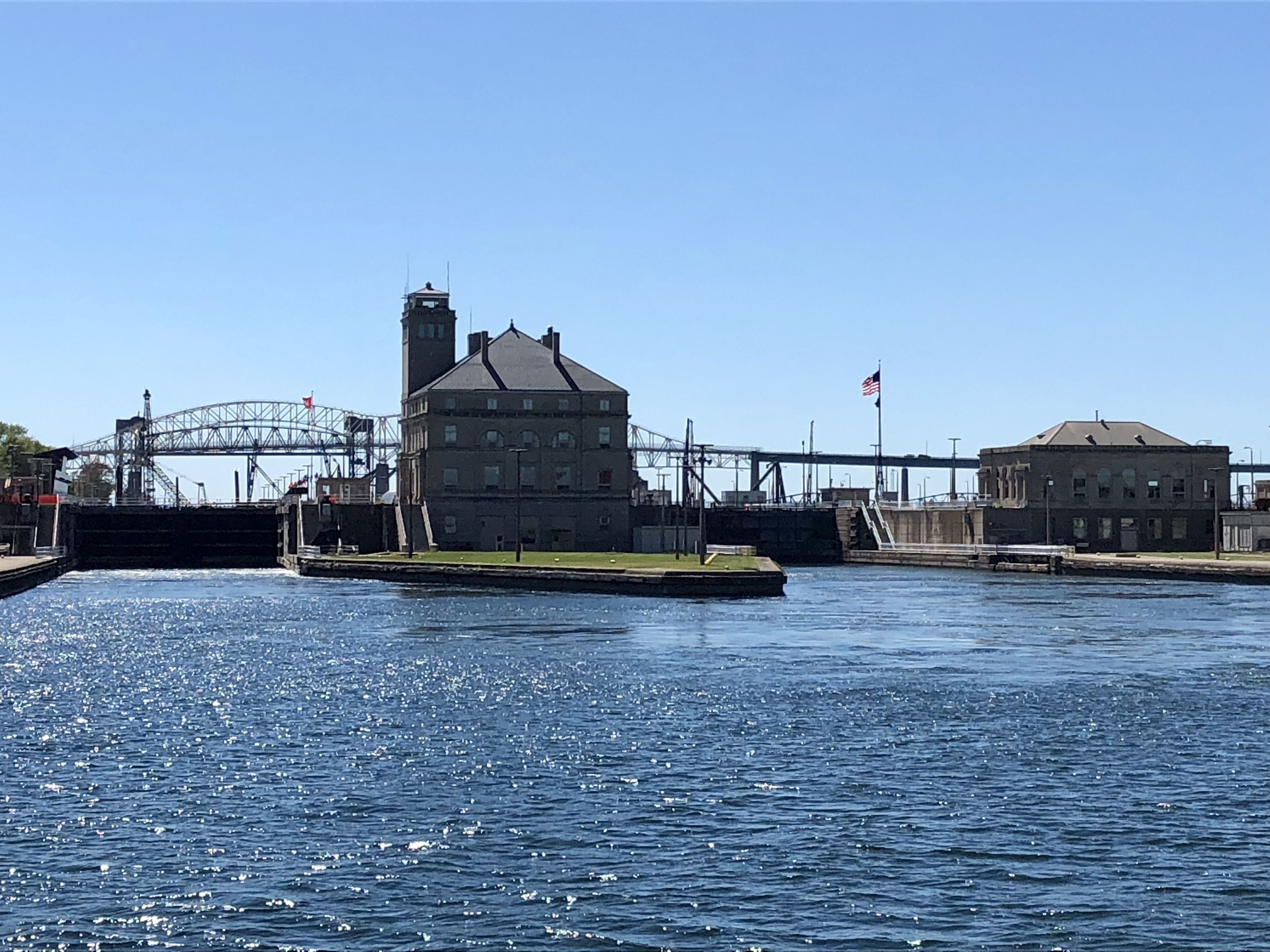 A waterfront building with a large waterway in front, a bridge in the background, and an American flag on a pole.