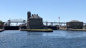 A waterfront building with a large waterway in front, a bridge in the background, and an American flag on a pole.