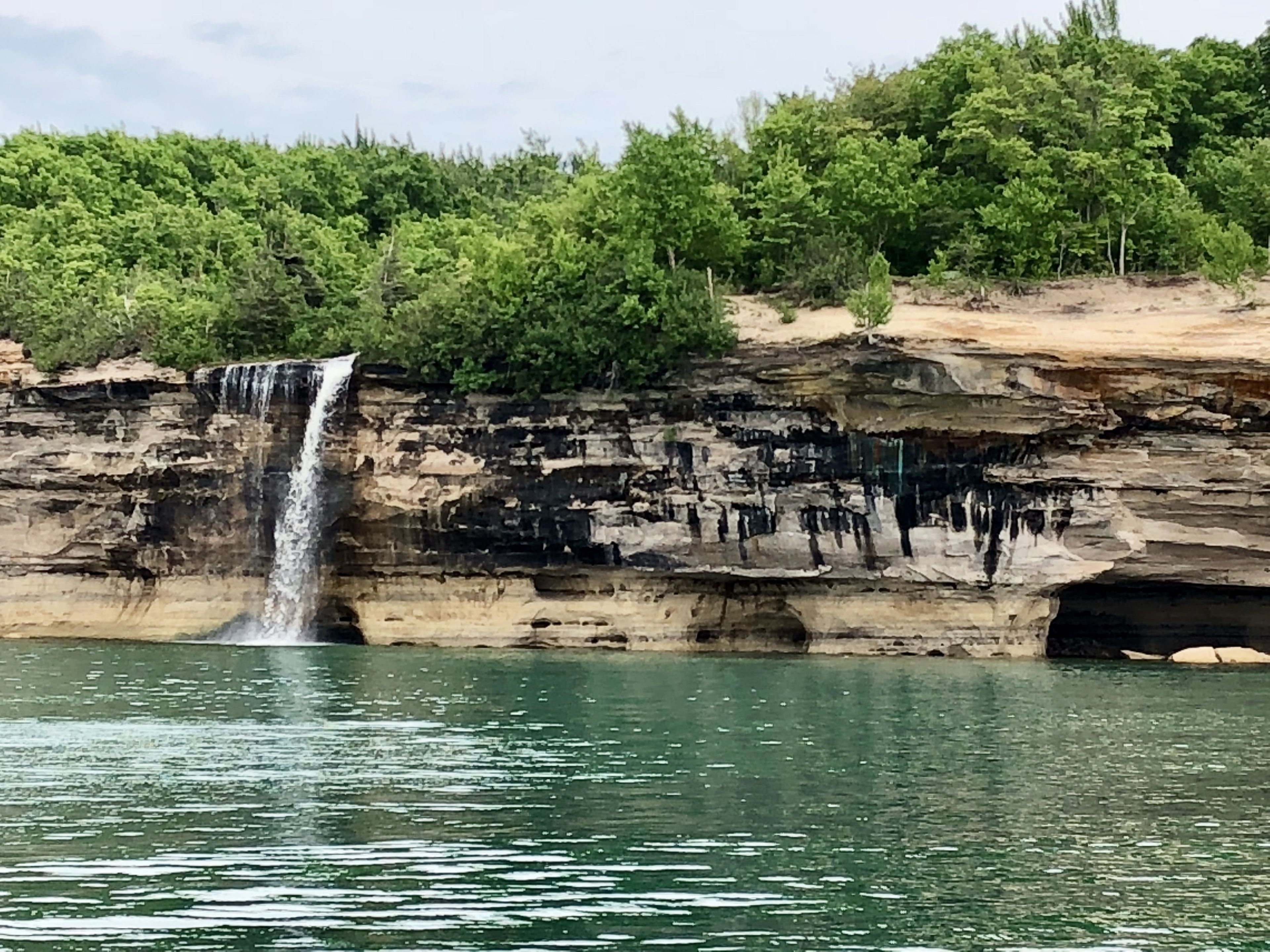 A waterfall cascading down a rocky cliff into a body of water, surrounded by dense greenery.