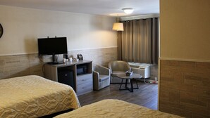 Quarto de hotel com duas camas, uma escrivaninha com televisão de tela plana, uma cadeira, uma mesa e uma janela com cortinas.