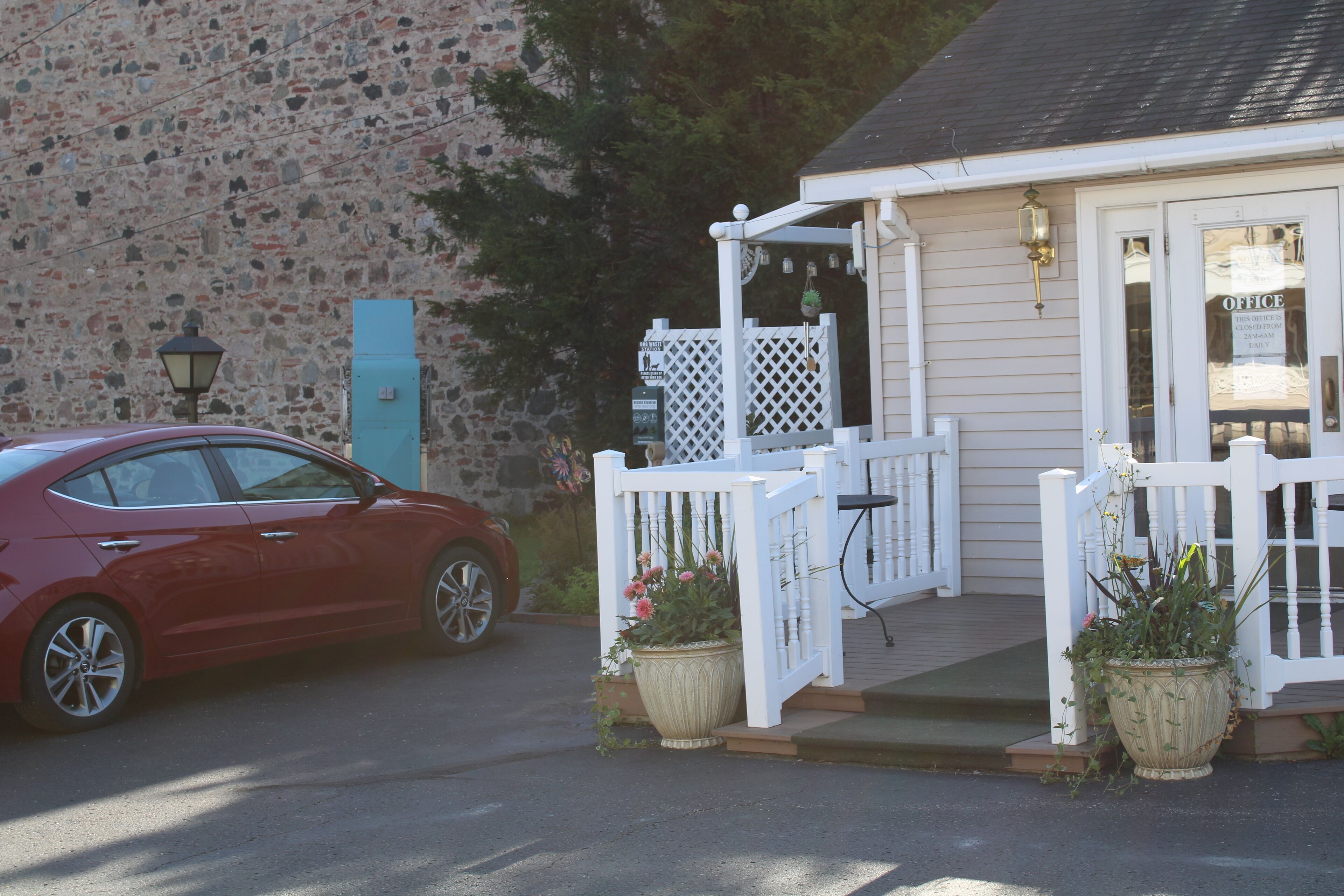A red car parked in front of a building with a white porch and a sign that reads "OFFICE".