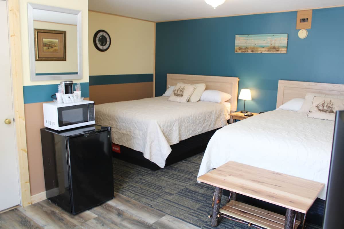 A hotel room with two beds, a microwave, a small desk, and a nightstand with a lamp.