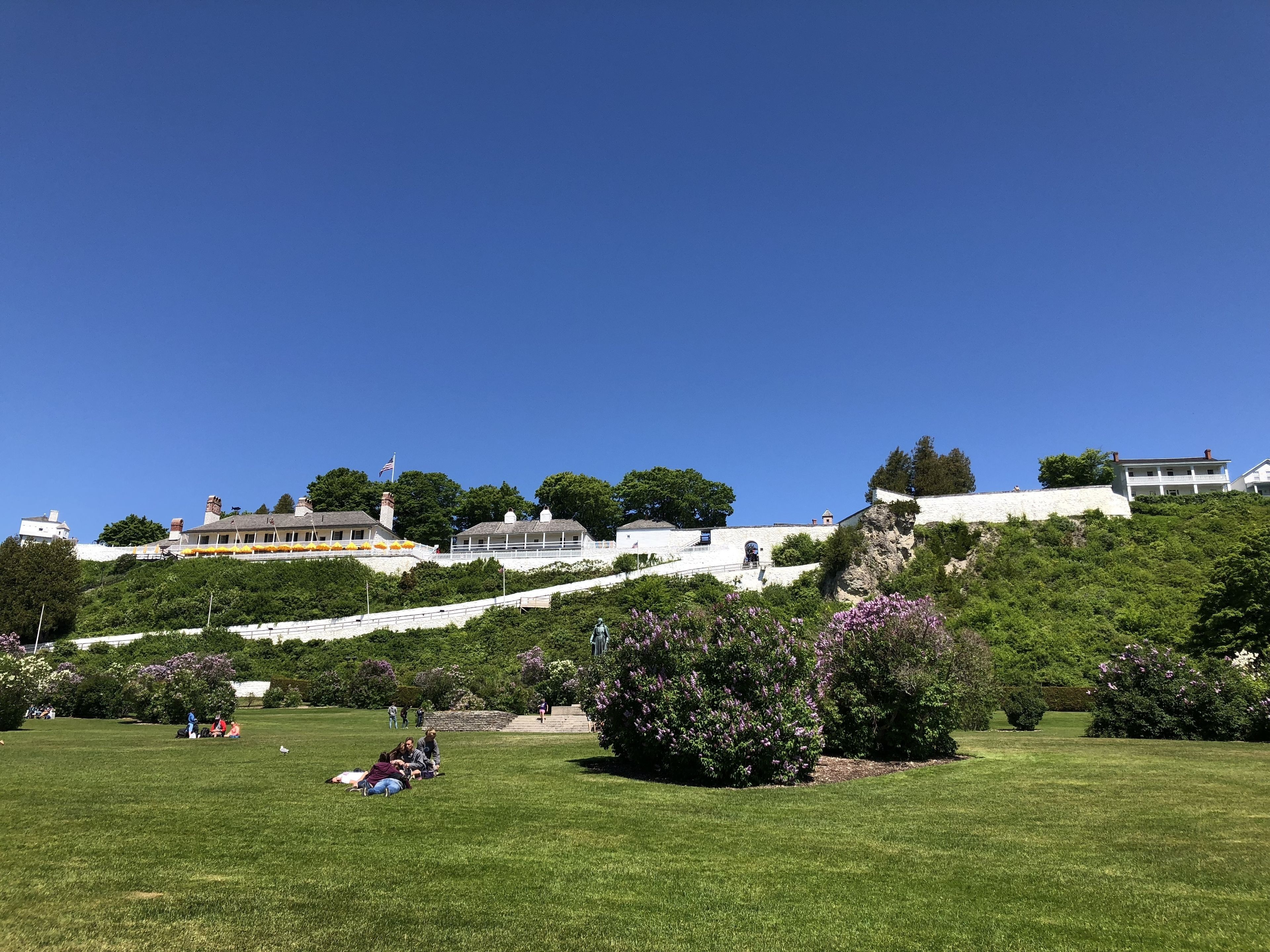 A park with grassy areas, trees, and a white building with a flag.