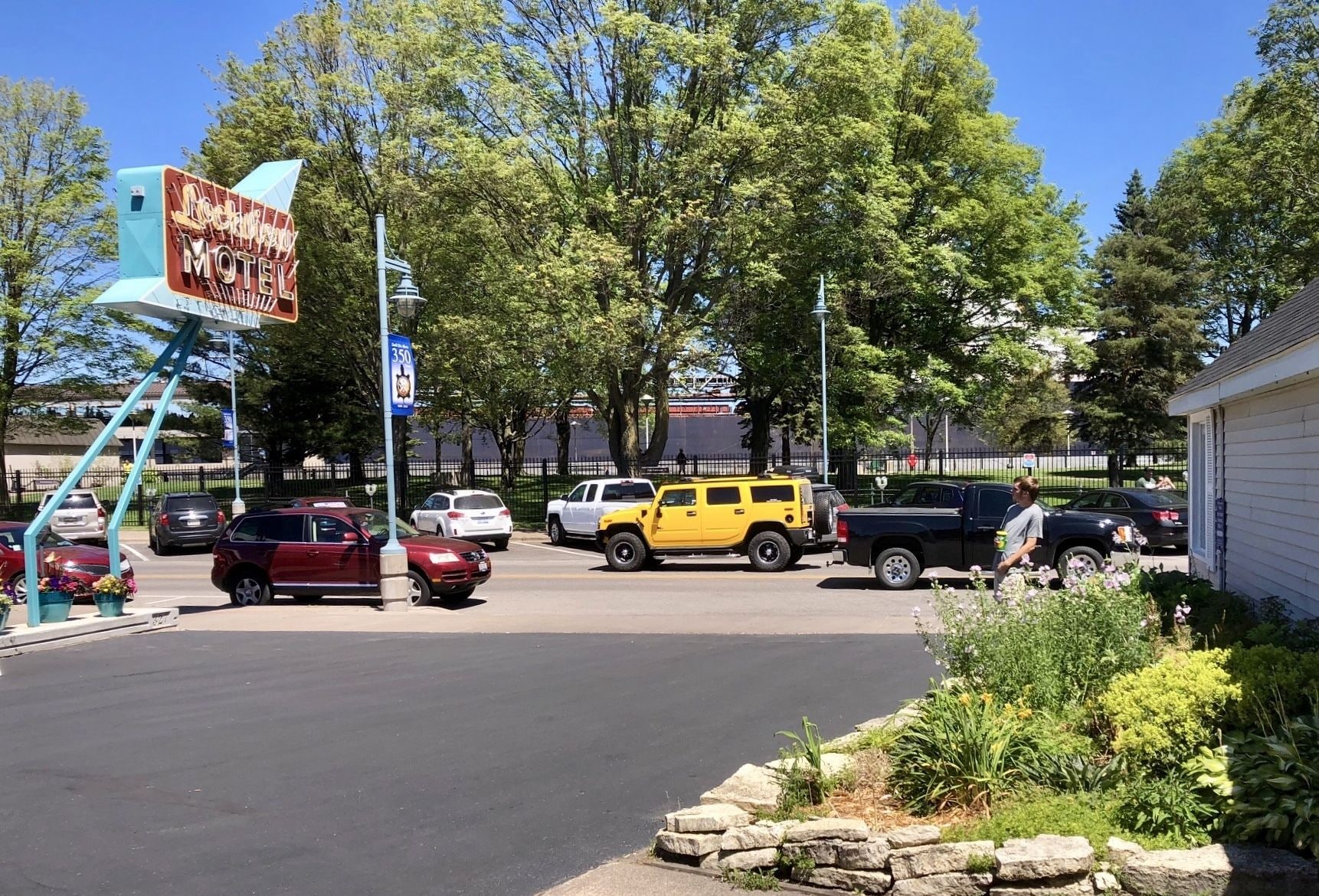 Letrero de motel, estacionamiento con varios vehículos y muro de piedra con plantas.