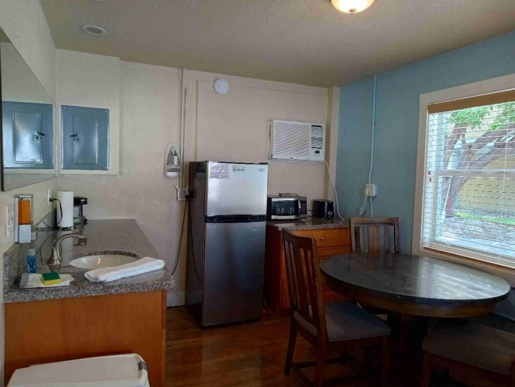 A compact kitchen with a refrigerator, microwave, sink, and a dining area with a table and chairs.