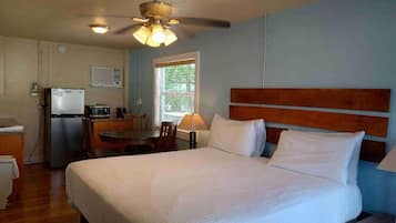 A hotel room with a bed, a desk, a refrigerator, and a ceiling fan.