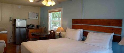 A hotel room with a bed, a desk, a refrigerator, and a ceiling fan.