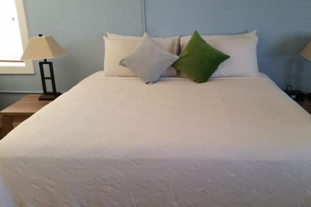 A neatly made bed with a white duvet, two bedside lamps, and a green pillow.