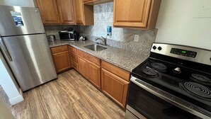 A kitchen with wooden cabinets, a stainless steel refrigerator, a granite countertop, a sink, a microwave, a stove, and a clock. - Knight's Key Suites (Marathon)
