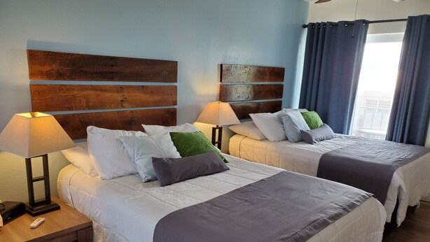 A hotel room with two beds, each with a wooden headboard, white bedding, and a bedside table with a lamp. - Knight's Key Suites (Marathon)