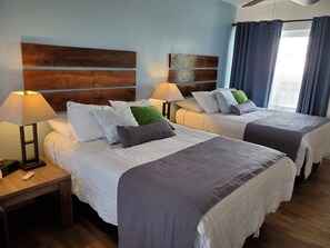 A hotel room with two beds, each with a wooden headboard, white bedding, and a bedside table with a lamp.