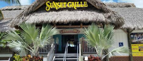 Un edificio con techo de paja y un cartel que dice 'Sunset Grille & Raw Bar'.