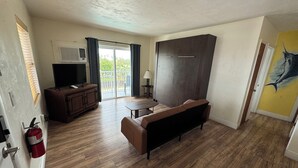 A spacious living room with a wooden floor, a sofa, a TV, a cabinet, and a sliding glass door leading to a balcony. - Knight's Key Suites (Marathon)