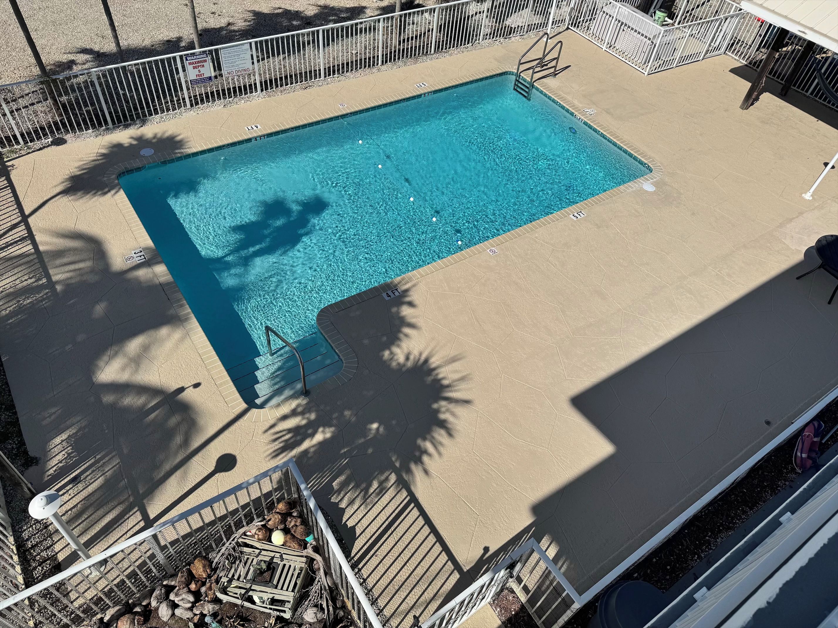 A rectangular swimming pool with a metal ladder and a safety sign.